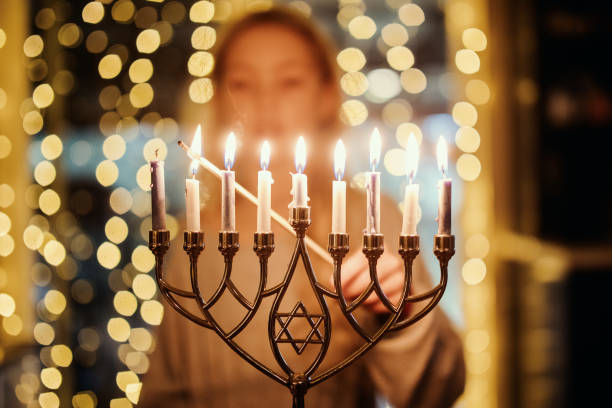 An elementary age child lighting the Menorah candles with a long match for Hanukkah celebration over the holiday.